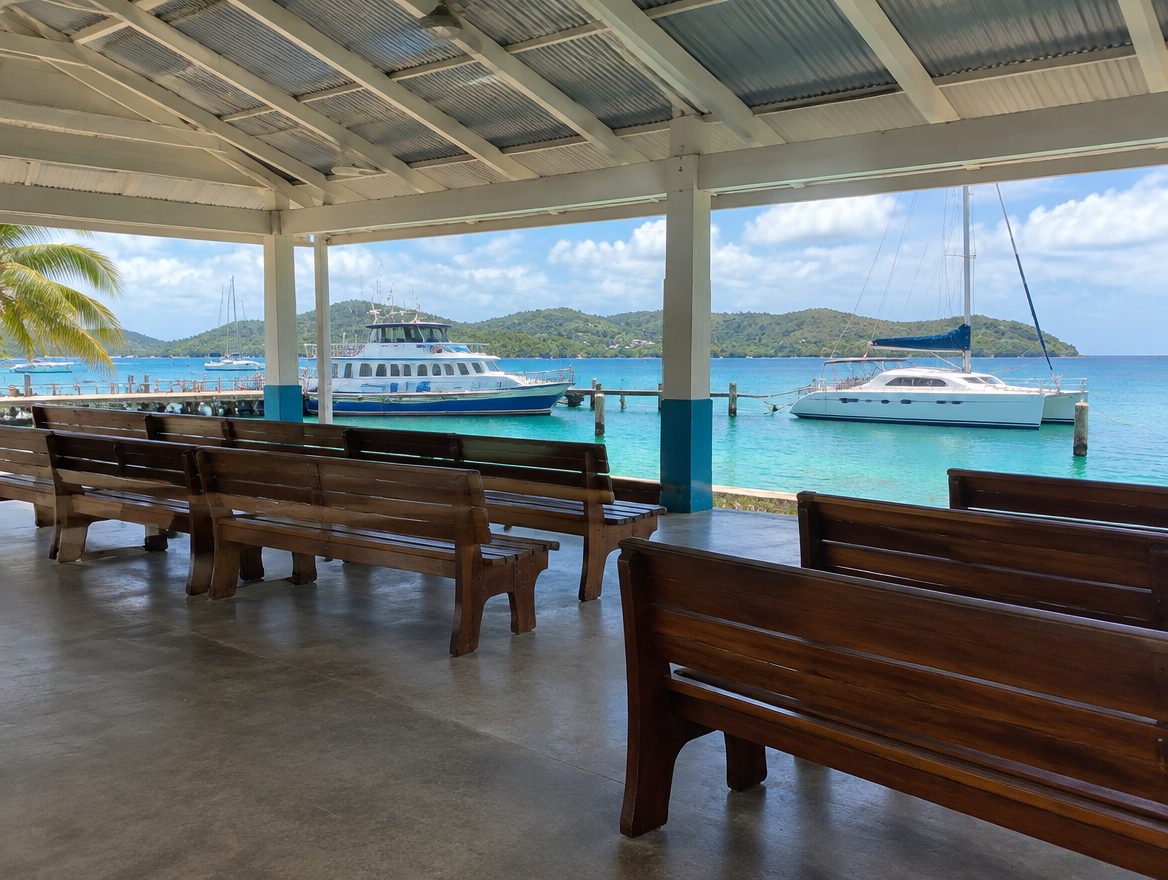 Open-air covered ferry terminal waiting area beside moored boats